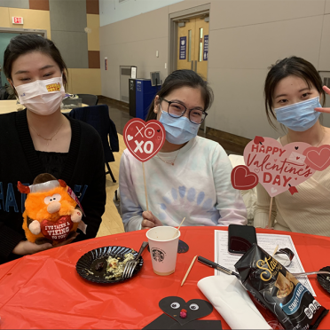 Three students in masks at a lunch table decorated for Valentine's Day