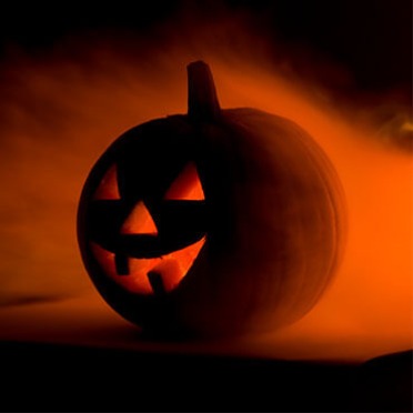 A spooky jack-o-lantern sits in the darkness with smoke billowing around it