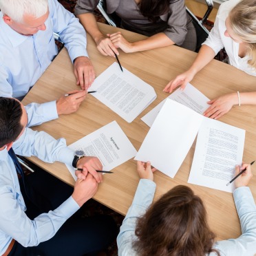 A group of faculty members review papers while drinking coffee