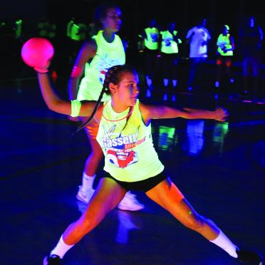 A female student poised to throw a dodgeball in the gym under blacklights