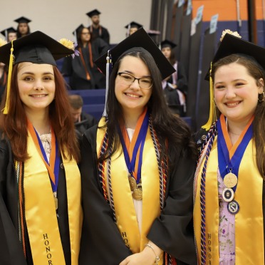 Three graduates pose with stoles and honor cords