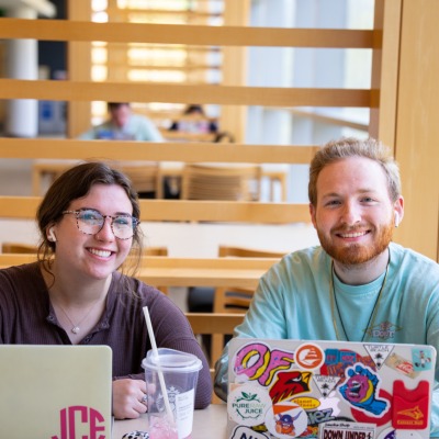 Two smiling students with laptops at a table in the library