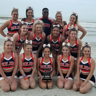A group of club cheerleaders in uniform pose on the beach