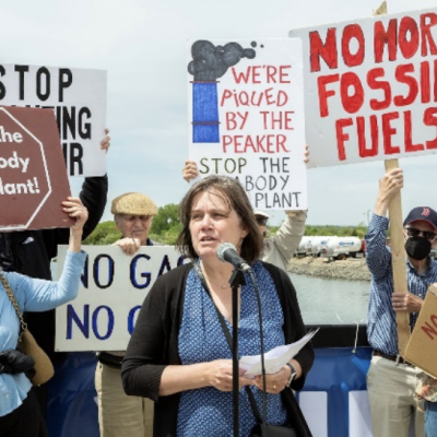 Depicted: a group of people protest behind a woman at a microphone. The protesters hold signs saying "No more fossil fuels", "Stop the Peabody gas plant!".