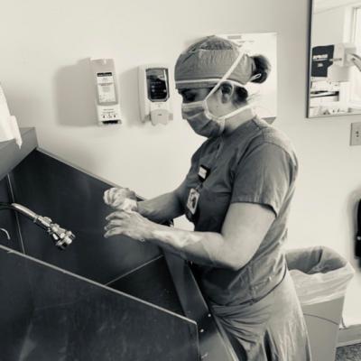 Ashley Bouchard, Winchester Hospital Registered Nurse and 2016 graduate of Salem State Nursing, washes her hands while in hospital scrubs in a black-and-white photo.