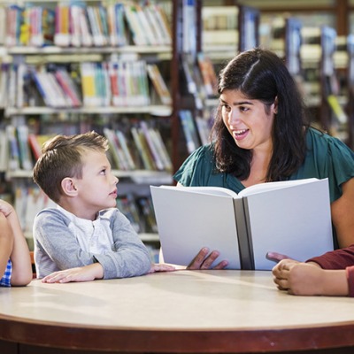 A female school librarian at a table with three young students