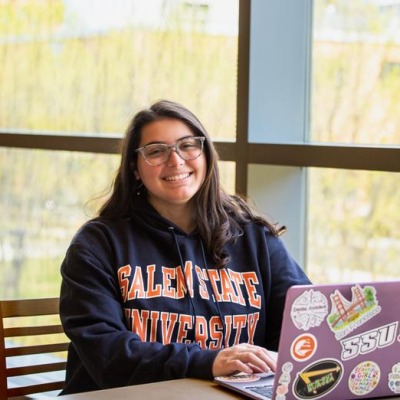 A student smiles from behind a laptop in the library