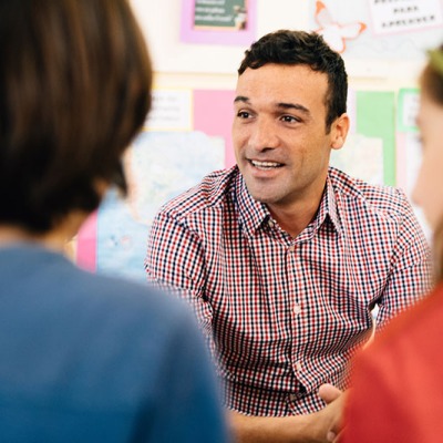 A male teacher smiles at two students