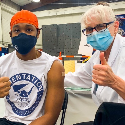 A student and a faculty nurse give a thumbs up after a COVID vaccine.