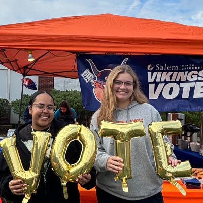 Two smiling student ambassadors outside the Enterprise Center with "VOTE" balloons