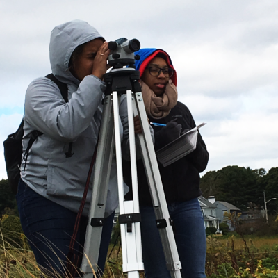 Two students outdoors looking through an instrument on a tripod