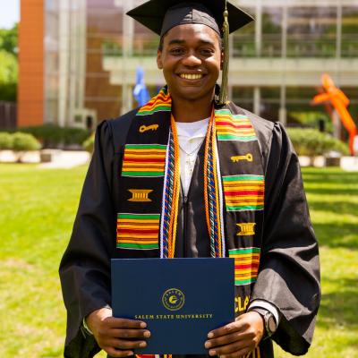 Salem State class of 2020 graduate stands in front of the library with his diploma cover.
