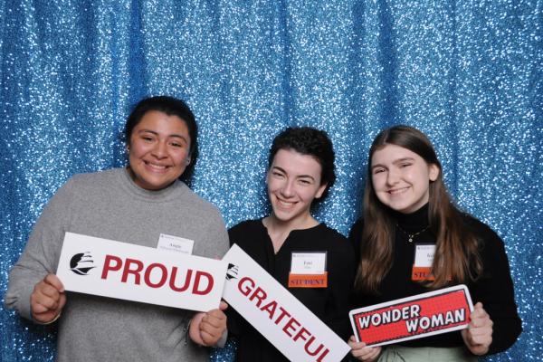 Three student scholarship recipients holding signs that read proud, grateful and wonder woman
