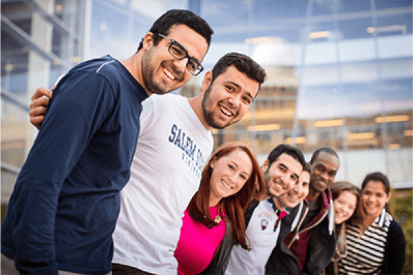 A group of students put their arms around each other in the campus quad, smiling at the camera 