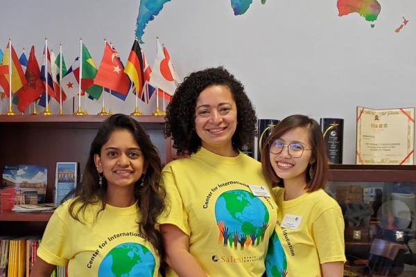 Three International students smile and wear "Center for International Education" shirts.