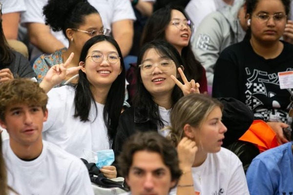 Two international students smile and do a peace sign. 