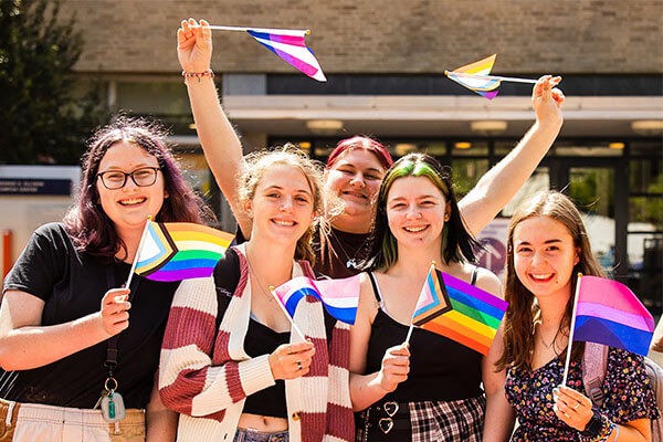 A group of students in Alumni Plaza waving pride flags and smiling gleefully