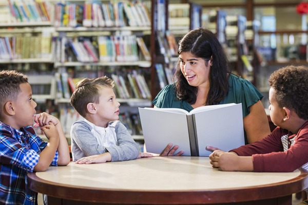 A female school librarian at a table with three young students