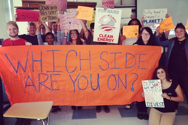 Students advocating for fossil fuel divestments hold painted signs on campus