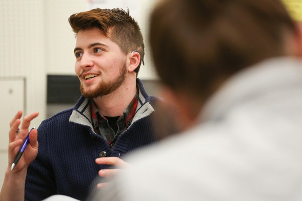 A male student in class gesturing and smiling