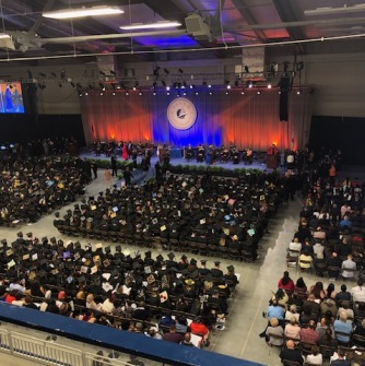 Graduates and guests seated at commencement ceremony; view from the bleachers