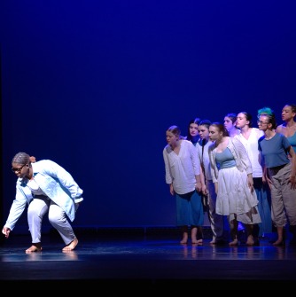 Dancer in white standing in front of a group of dancers on stage