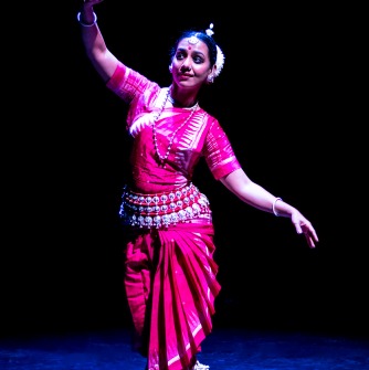Priya Bangal dressed in a pink costume with arms extended on a stage