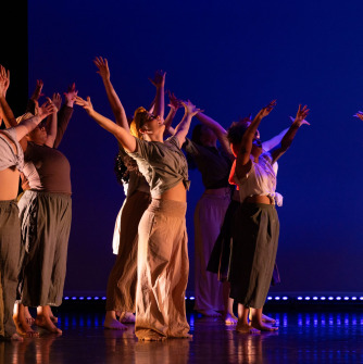 A group of dancers with arms raised in front of a blue background