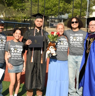 Graduate with family and President Keenan posed on athletic field after commencement ceremony