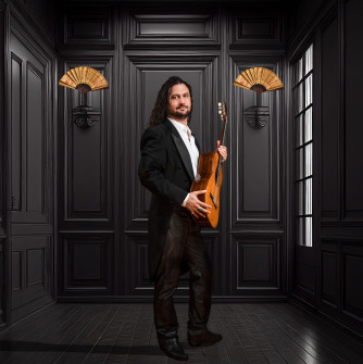 Man dressed in black holding a guitar and standing in a black room