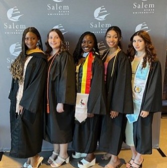 Graduates posed standing together in cap and gown in front of Salem State photo backdrop