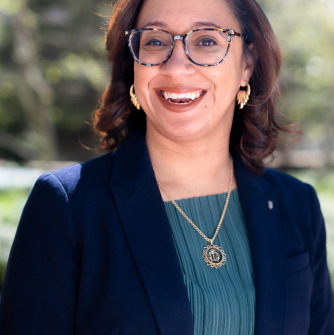 Sophia Hall headshot. Woman smiling with glasses and brown hair, wearing black blazer and blue shirt.