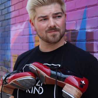 Man with spiky blond hair, black shirt and tap shoes hanging around his neck