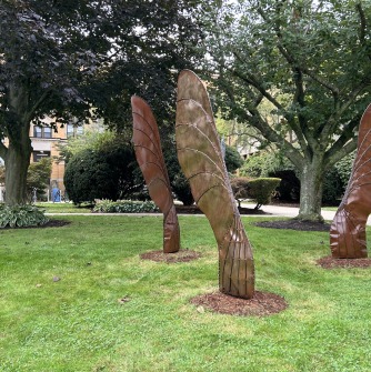 Metal sculptures of three seeds from a gigantic tree, standing upright in front of Salem State University's Sullivan Hall