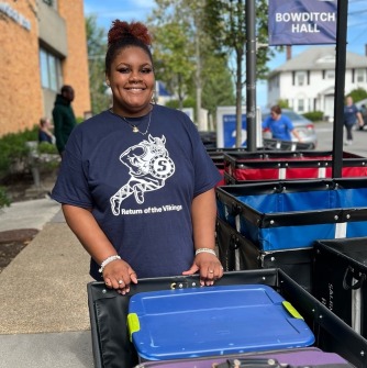 A smiling student with a move-in cart outside Bowditch Hall during move-in weekend