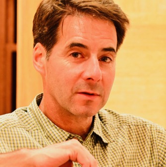 Man in greenish shirt in front of a yellow background