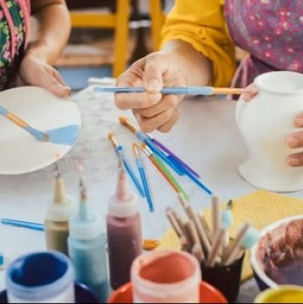 Two people using paintbrushes to paint pottery