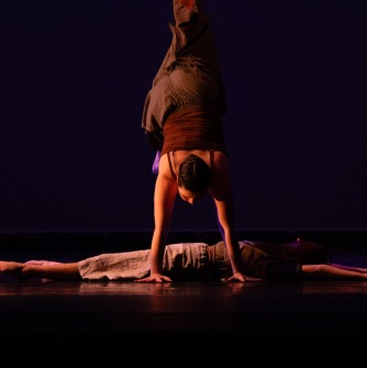 Dancer on floor while another dancer does a handstand in front of them