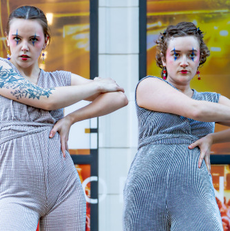 Two dancers in gray with their right arms across their bodies