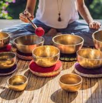 A person is sitting cross-legged on a mat surrounded by sound bowls.