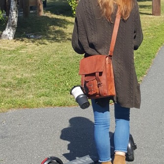 Woman wearing helmet rides scooter on bike path.