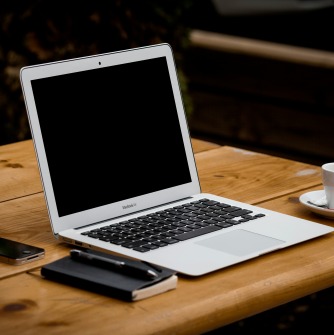Image of a laptop on a table with a phone, notepad, and cup of coffee