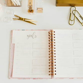 Notebook with the word goals on it, with office/desk supplies scattered around it