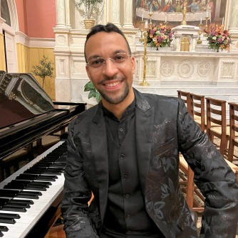 Javier Marquez sitting on a bench at a piano in a black suit