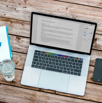 Table with laptop, notepad/pen, cell phone, and glass of water on it.