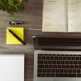 Image of a laptop, planner, sticky note, pen and spiral notebook on a desk