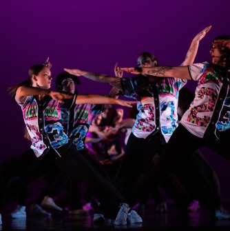 Dancers in brightly colored shirts looking at each other