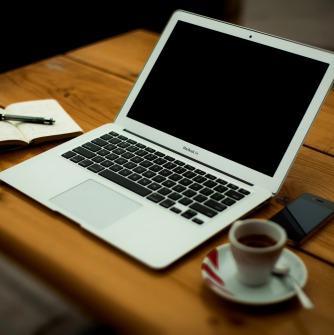 Laptop with open notebook, phone, and coffee cup