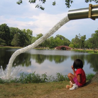 Child squatting in front of a large sculptural faucet with water coming out