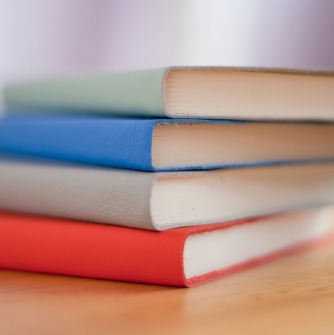 Stack of books (green, blue, white, and orange) stacked on desk